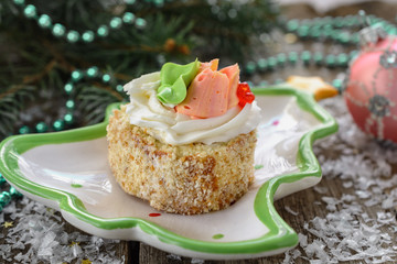 Delicious New Year's biscuit cake with butter cream, decorated with flowers from the cream is on a porcelain plate a plate shaped like Christmas tree next to Christmas balls and beads, close up