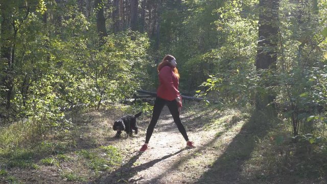 A young athletic girl walks with a dog in the woods and engaged in sports exercises and gymnastics in the forest glade, which is illuminated by the sun. 4K. 25 fps.