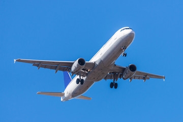 Fototapeta na wymiar A white airplane flying in a clear pale blue sky