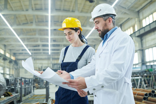 Side view portrait of female factory worker discussing work with mature engineer holding plans