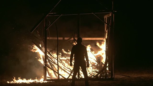 A man stands at a burning house, a man against a burning house at night, Overall plan
