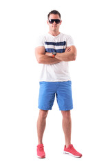 Serious tough young man in shorts and sunglasses with crossed arms. Full body isolated on white background. 