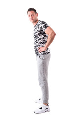 Fototapeta premium Side view of indifferent expressive young adult man in army shirt and sport clothing looking at camera. Full body isolated on white background. 