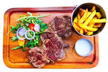 Beef steak with fried potatoes, sauce and arugula at wooden desk