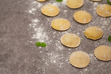 Tasty raw ravioli with flour on dark background. Process of making italian ravioli.
