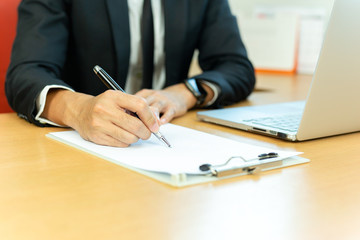 Businessman signing contract paper with pen and laptop in office desk.