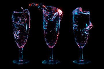 Water colorfully glowing and splashing from three champagne tulip glasses in a row on a black background