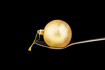 Golden shiny ball Christmas toy on a spoon isolated on black background