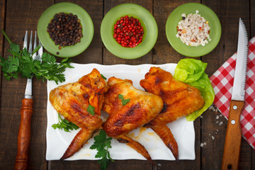 Grilled chicken wings with spices and herbs on dark background, top view.