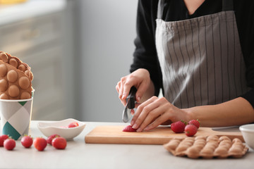 Woman cutting fresh strawberry for filling bubble waffles in kitchen