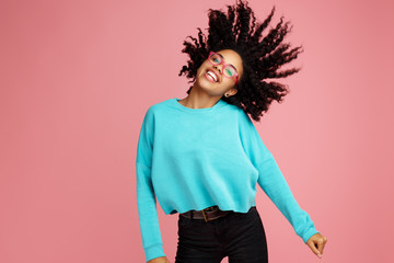 Excited african american young woman with bright smile dressed in casual clothes, glasses and headphones dance over pink background. - Powered by Adobe