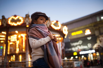 Child girl is walking at the street against background of evening city lights.