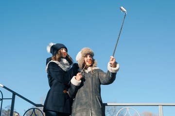 Two young teenage girls having fun outdoors, happy smiling girlfriends in winter clothes taking selfie, positive people and friendship concept.