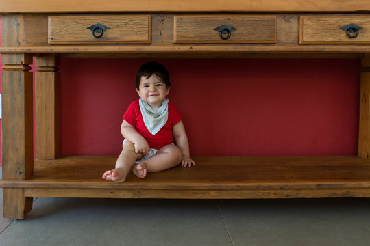 Beautiful baby sitting under a wooden cupboard with red background