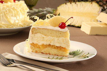 Macro close up of appetizing white chocolate cake with pineapple and cherry with out of focus cake in background.