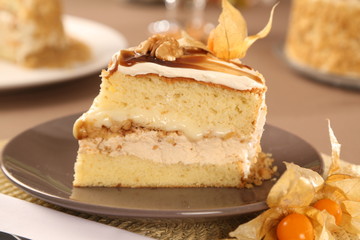 Macro close up of appetizing slice of white chocolate cake with nut and Physalis with out of focus cake in background.