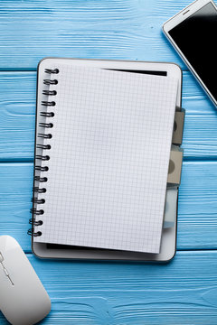 Notebook on digital tablet, white smartphone and computer mouse on wooden table