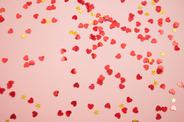 Defocused beautiful hearts and stars shaped red confetti on pink background.