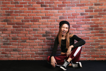 Fototapeta na wymiar Photo of beautiful young hip hop dancer or sporty girl, sitting on floor against brick wall