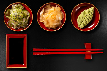 Sunomono, ginger, wasabi, hashi and shoyu isolated on black background. top view.