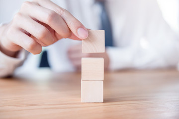 Hand of businessman arranging empty wood cube stacking on top with wooden table. Space for symbol.