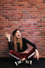Fototapeta na wymiar Photo of happy hip hop dancer or sporty woman, sitting on floor against brick wall