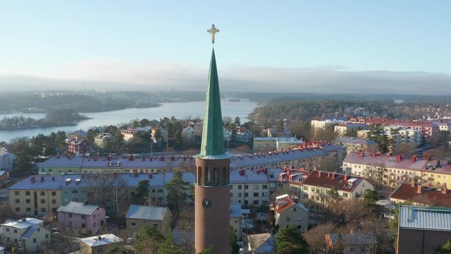 Aerial footage of the Stora Essingen church tower with a golden christian cross on top in Stockholm, Sweden