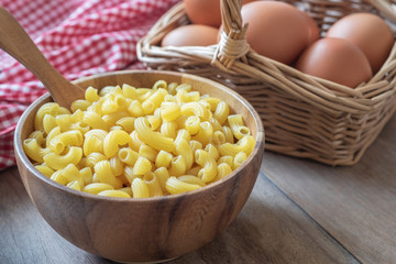 Raw macaroni pasta in wooden bowl and egg in basket