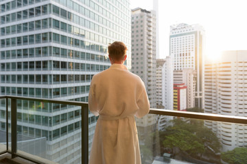 Young handsome man enjoying the view of the city from the balcon