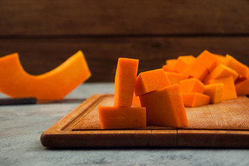 Pieces of orange pumpkin on a wooden Board. Light background. Raw vegetables. Vegetarian food.