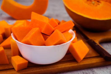 Sliced pumpkin cubes in a white bowl. Orange flesh of ripe fruit. Vegetarian food. Raw vegetables.