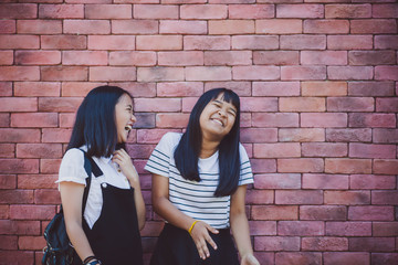 Obraz na płótnie Canvas two asian teenager laughing with happiness emotion standing against red brick wall