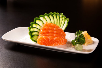 sashimi with salmon in a white plate. On a black background.