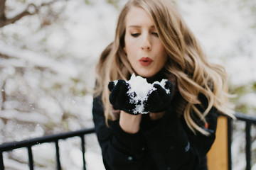 Beautiful Young Woman Modeling Bundled in Trendy Gloves, Coat, and Scarf Smiling and Having Fun With Snow Outside in Nature Around White Trees in the Cold Winter