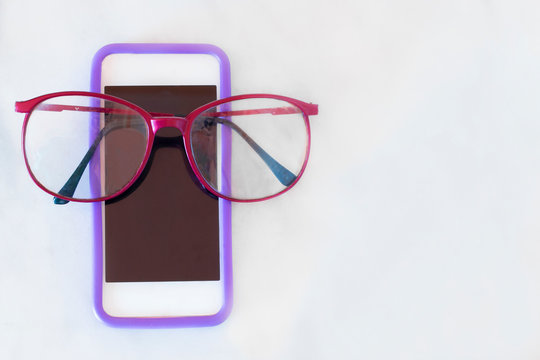 Red eye glasses sitting on a smartphone on a solid white background
