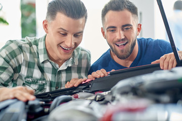 Handsome clients looking under hood of powerful vehicle. 