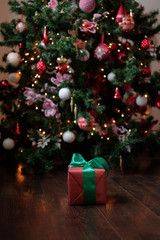 The gift lies on a dark wooden floor under the Christmas tree with a glowing gerland.