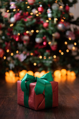 The gift lies on a dark wooden floor under the Christmas tree with a glowing gerland.