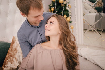 Young happy couple in love hugging.Young man and woman celebrate Christmas holidays together in a bright bedroom decorated for xmas. Merry Christmas and Happy New Year 2019 Holidays concept
