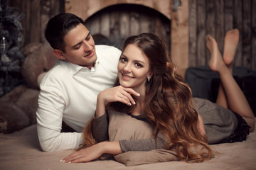 Young happy couple in love lying on rug in cozy wooden interior. Beautiful brunette woman with boyfriend enjoying.