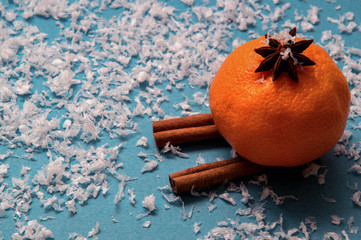 Orange mandarine in aniseed hat skiing out of cinnamon. Deep blue background with artificial snow. Copy space.