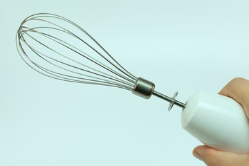 metal whisk mixer for beating in hand, on blue background, close-up