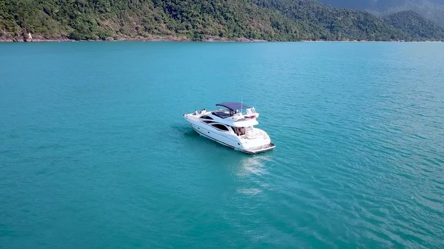 Yacht motorboat floating in blue tropical sea water near island coastline, drone aerial footage turning around the boat, beautiful landscape, vacation holiday leisure