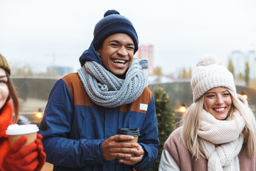 Happy young friends talking with each other drinking coffee outdoors winter concept.