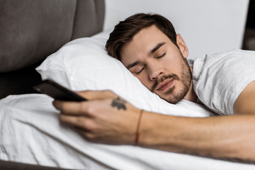 handsome bearded young man sleeping in bed with smartphone in hand