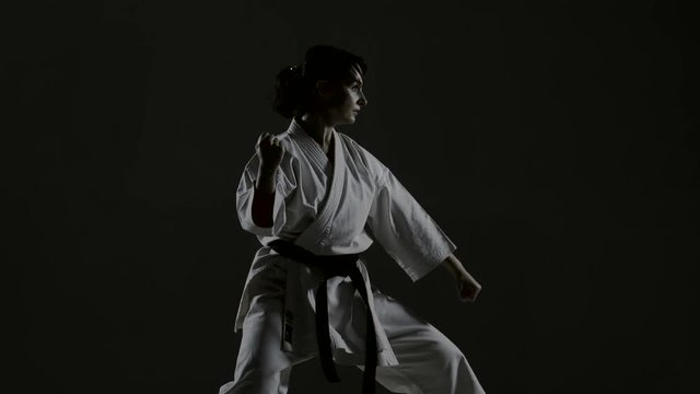 girl practicing karate, wearing kimono, harsh side light against black background