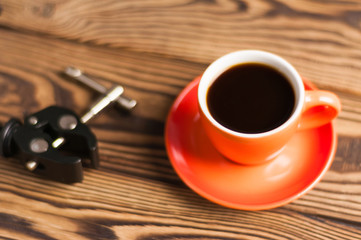 Black metal arm near orange ceramic mug full of black coffee on old wooden brown table