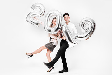 Funny girl and guy dressed in a stylish smart clothes are holding balloons in the shape of numbers 2019 on a white background in the studio