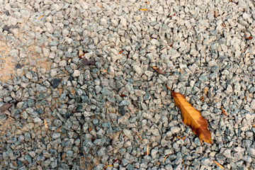 Gravel textured.  .Pile of gravel laying on earth ground with brown leafs on top and sunlight ,high angle view..