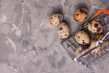 Spotted fresh quail eggs poured out of metal glossy market basket on old broken worn gray cement...